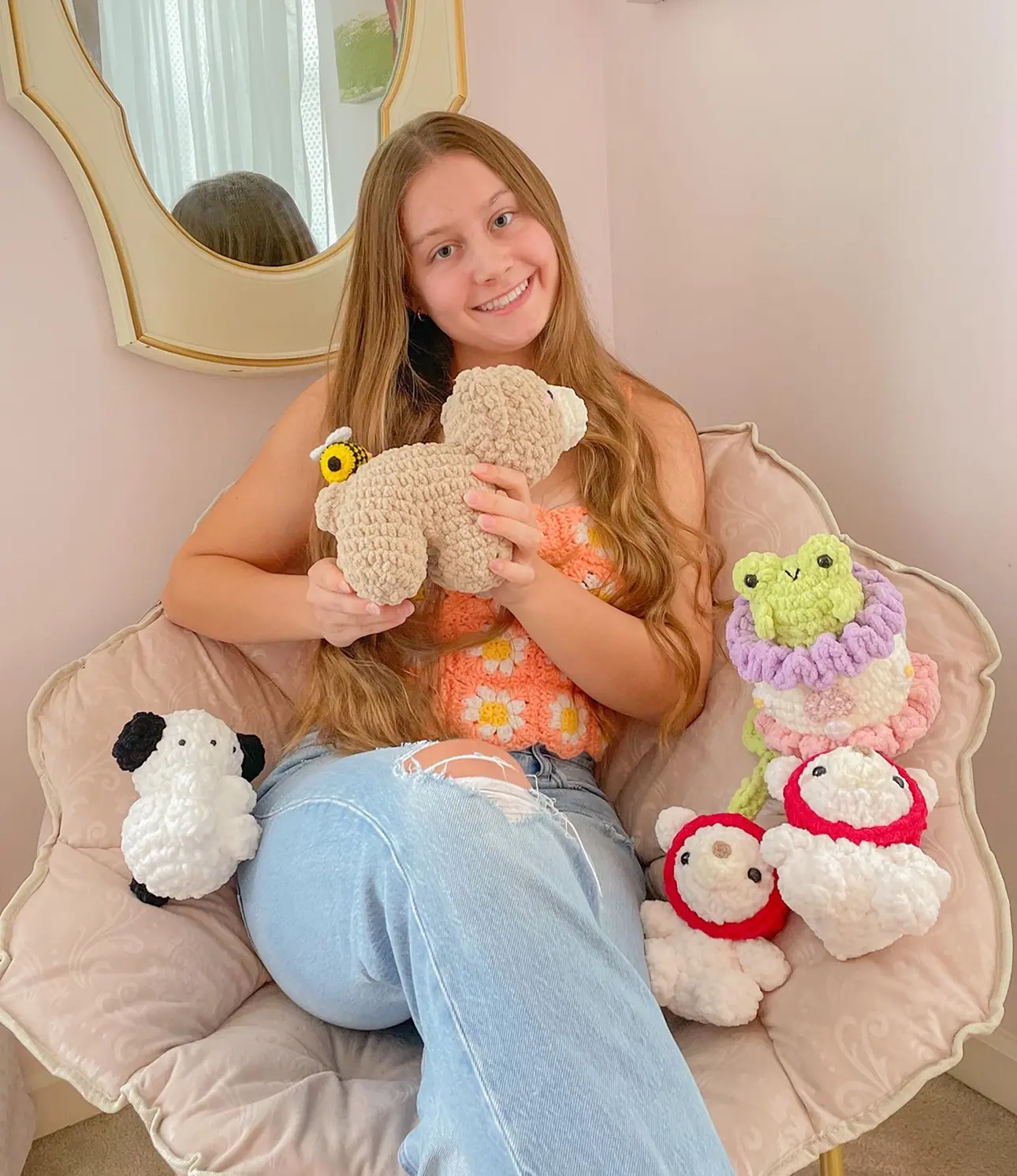 Scarlet sitting in a chair holding a crocheted teddy bear, surrounded by other crocheted plushie animals